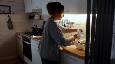 Sıcak ve davetkar bir mutfakta, bir kadın lavaboda bulaşıkları yıkar. Yumuşak ışıklandırma, akşam işlerini dikkatle yaparken sakinleştirici bir atmosfer yaratıyor..