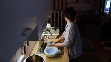 Sıcak bir mutfakta, bir kadın evdeki eşyalarla çevrili olarak lavaboda bulaşık yıkar ve organize eder. Akşam çöktüğünde ortam sakin ve davetkar geliyor..