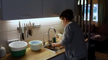 Sıcak bir mutfak ortamında, bir kadın yemekten sonra bulaşıklarla meşgul olur. Yumuşak ışıklandırma, temizlik yaparken davetkar atmosferi güçlendiriyor. Daha sonra bir aile toplantısı için hazırlanıyor..