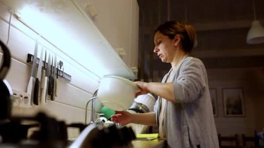 Sıcak bir mutfakta, bir kadın tezgahta yemek hazırlamaya odaklanır. Çeşitli mutfak aletleri kullanıyor, bir gecelik mutfak aktivitesi sergiliyor..