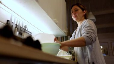 İyi aydınlatılmış bir mutfakta, bir kadın bulaşıkları yıkar, günlük ev işlerini gösterir. Verimli bir şekilde lavabo kullanıyor ve pozitif tavrını sürdürürken alanı düzenli tutuyor..