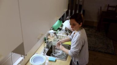 Bir insan sıcak ve davetkar bir mutfakta bulaşıkları yıkıyor. Atmosfer sakin ve rahat, yumuşak ışıklandırma akşam yemeğinden sonra temizlik rutinini artırıyor..