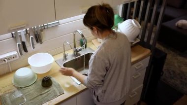 Bir insan sıcak ve davetkar bir mutfakta özenle bulaşıkları yıkar. Lavabo kabarcıklarla dolu. Akşamın ilerleyen saatlerinde arkadaşlarıyla akşam yemeği için hazırlanıyorlar..