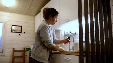 Sıcak ve davetkar bir mutfakta, bir kadın neşeyle çay hazırlarken görülüyor. Yumuşak ışıklandırma, büyüleyici bir kır evinde akşam rutininin tadını çıkarırken rahatlatıcı bir atmosfer yaratıyor..