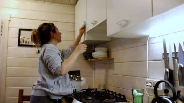 Bir insan kırsal bir kabindeki mutfak dolaplarını temizlemeye odaklanır. Neşeli atmosfer, pencereden akan doğal ışıkla güçlenir..