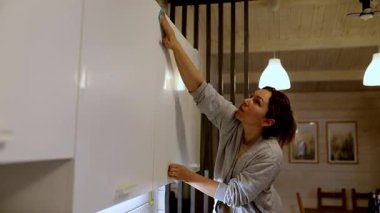 Bir kadın modern bir evde mutfak dolaplarını özenle temizlerken görülüyor. Akşam ışığı boşluğu doldururken her şeyin lekesiz olmasını sağlıyor..