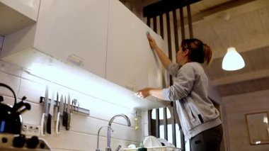 Sıcak, modern bir mutfakta, insan akşam temizliğinin bir parçası olarak mutfak dolaplarını düzenler ve düzenler. Sıcak ışıklandırma evin davetkar atmosferine katkı sağlar..