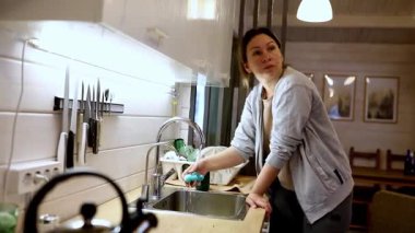 İyi aydınlatılmış bir mutfakta, bir kadın mekanını düzenlerken bulaşıkları yıkamaya odaklanır. Yaklaşan aile toplantısına hazırlanıyor. Her şeyin düzenli ve misafirperver olmasını sağlıyor..