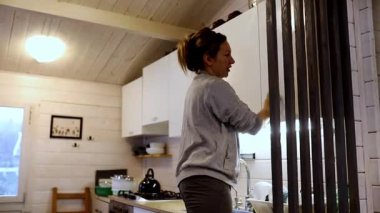 Büyüleyici bir kamara ortamında, bir kadın mutfağı düzenlerken sıcak ışık boşluğu dolduruyor. Bulaşıkları düzenler ve güne barışçıl bir başlangıç hazırlar..