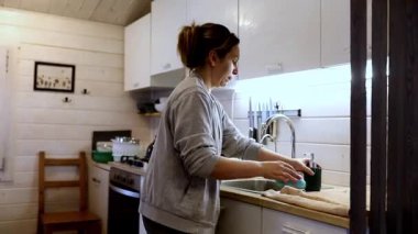 Bir kadın, rahat bir kabin mutfağında bulaşıkları yıkıyor, sakin atmosferin tadını çıkarıyor. Güneş ışığı boşluğu dolduruyor, öğleden sonraki ritüelin sakinliğini arttırıyor..