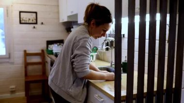 Sıcak ve davetkar bir mutfakta bir kadın tezgahı temizlemeye odaklanır. Yumuşak ışıklandırma, rahat atmosferi güçlendiriyor. Sabah işleri için huzurlu bir ortam yaratıyor..