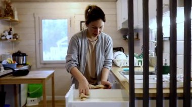 Sıcak bir mutfakta bir kadın çekmeceleri düzenler ve yemek malzemeleri hazırlar. Davetkar atmosfer, sıcak bir ev ortamının ve gıda hazırlıklarında detaylara dikkat edildiğinin altını çiziyor..