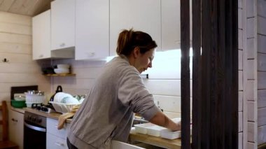 Sıcak bir mutfak ortamında, bir kadın yemekten sonra bulaşıkları ve çatal bıçakları özenle temizler. Odaklanmış ve düzenli görünüyor, düzenli bir yemek alanı yaratıyor..