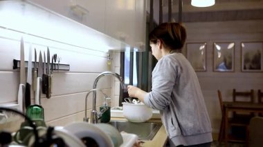 Şık bir mutfakta, bir kadın çalışma alanını düzenler ve yemek malzemeleri hazırlar. Sıcak ortam ve şık aletler yemek hazırlamak için hoş bir ortam yaratıyor..