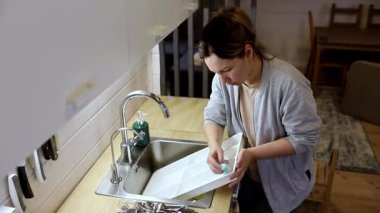 Sıcak bir mutfak ortamında, bir kadın lavaboda bulaşıkları yıkar ve düzenler. Sıcak atmosfer rahatlatıcı bir hava yaratıyor. Günlük rutin ve evde bakım için mükemmel bir ortam..