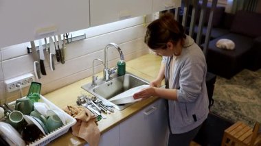 Bir kadın, temiz ve modern bir mutfakta özenle bulaşıkları yıkıyor. Tabakları ve çatal bıçakları dikkatlice temizler, günlük işlerini yaparken düzenli bir çalışma alanı sağlar..