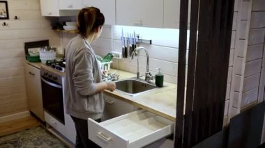 Bir kadın modern bir kulübede mutfak çekmecesini karıştırıyor. İyi ışıklandırılmış alanda ahşap aksanlar var. Kolayca ulaşılabilecek alet ve gereçleri dikkatlice düzenliyor..