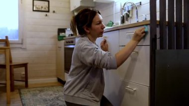 Bir kadın, kırsal bir evde mutfağını özenle temizleyip düzenlerken görülüyor. Bir bez kullanarak mutfak dolaplarını temizler ve düzenli bir yaşam alanı sağlar..