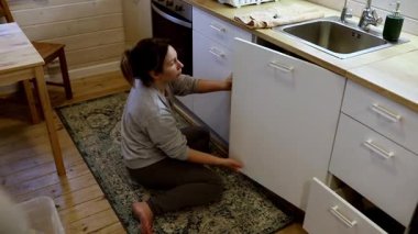 Bir insan yerde diz çöküyor, mutfak dolaplarını sıcacık yanan bir ahşap evde ovuyor..