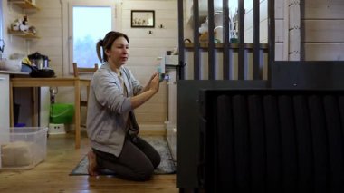 Bir kadın kırsal bir kulübede yere çömelmiş, özenle mobilya montajı yapıyor. Doğal ışık pencerelerden akar ve davetkar atmosferi güçlendirir..