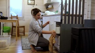 Bir kadın rahat, kırsal bir mutfakta mutfak eşyaları düzenlemeye odaklanır. Sabahları doğal ışık içeri dalarken çekmeceleri düzenler ve sakin bir atmosfer yaratır..