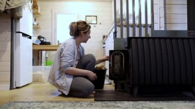 Büyüleyici bir kamarada, bir kadın odun sobasının yanına çömeliyor, ateşi dikkatlice ayarlıyor. Sıcak atmosfer onun rahatlık ve rahatlamaya olan ilgisini vurguluyor..