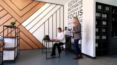 İki profesyonel şık bir ofis ortamında birlikte çalışırlar. Biri dizüstü bilgisayarla masada otururken, diğeri yakınlardaki belgeleri inceliyor..