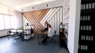Çağdaş bir ofis alanında şık bir masada çalışırken iki profesyonel tartışmalara giriyor. Kurulum, ilham ve takım çalışmasını desteklemeye odaklanıyor.