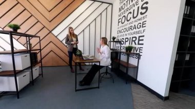 İki profesyonel, modern tasarım ve motivasyon alıntılarının yer aldığı çağdaş bir ofis ortamında fikirleri ve görüşleri paylaşıyor..