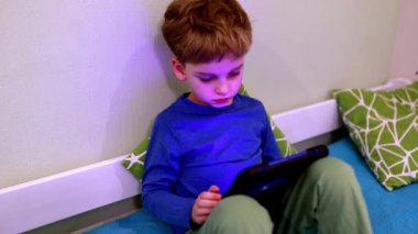 Genç bir çocuk yerde rahatça otururken bir tablete odaklanır. Odada yumuşak yastıklar ve sakinleştirici bir dekor var. Öğrenmek için davetkar bir atmosfer yaratıyor..