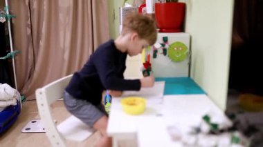 Küçük çocuk bir masada oturmuş, yaratıcı bir proje üzerinde çalışırken bir kase abur cuburun tadını çıkarıyor. Canlı oyun alanı oyuncaklar ve renkli dekorasyonlarla dolu..