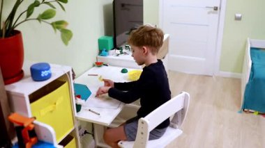 Genç bir çocuk, neşeli bir odada düzenli bir çalışma alanında yaratıcı sanat ve zanaat projesine girişiyor. Hayal gücü ve keşiflerle dolu bir öğleden sonra..