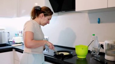 Bir kadın, parlak ve modern bir mutfakta krep hazırlıyor. Malzemeleri ve saatleri ustalıkla karıştırıyor hamurun fırında pişmesini izliyor ve nefis bir kahvaltı tabağı hazırlıyor..