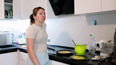 Kadın modern bir mutfakta ustalıkla krepleri kızartma tavasında çevirirken kaselerde malzemeler hazırlıyor ve yemek pişirme sürecinin tadını çıkarıyor..