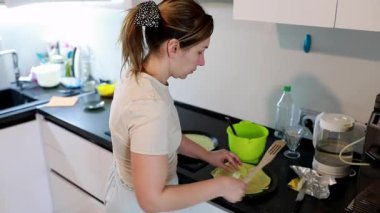 Parlak bir mutfak ortamında, bir kadın yemek pişirmeye odaklanır. Malzemeleri ve ekipmanları idare ediyor, rahat bir atmosferde aşçılık yeteneklerini sergiliyor..