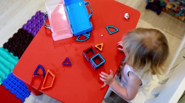 Genç bir çocuk şeffaf bloklardan renkli şekiller oluşturmaya odaklanır. Sıcak bir oyun odasında neşeli kırmızı bir masa üzerinde. Hayal gücünü ve yaratıcılığını sergiler..