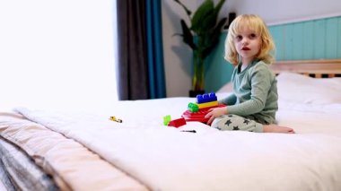 Genç bir çocuk bir yatakta otururken renkli bloklarla dolu bir binada mutlu mesut oturuyor. Davet odası doğal ışıkla dolu, sıcak bir atmosfer yaratıyor..