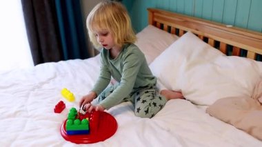 Küçük bir çocuk, ışıkla çevrili yumuşak bir yatakta renkli yapı taşlarıyla neşeyle oynar. Etkinlik yaratıcılığı ve hayal gücünü sıcak ve davetkar bir ortamda teşvik eder..