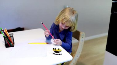 Bir çocuk kağıt üzerine resim çizmek için renkli kalemler kullanarak yaratıcı faaliyetlere girişir..