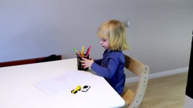 Genç bir çocuk parlak, neşeli bir mutfak masasında renkli kalemler kullanarak yaratıcılığı keşfeder. Oturum hayal gücünü ve oyunu ön plana çıkarıyor..