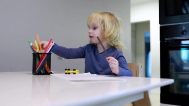 Genç bir çocuk mutfak masasında yaratıcılığı keşfeder, tutucudan canlı işaretler seçer. Oda parlak ve modern, sanatsal oyun ve hayal gücünü teşvik ediyor..