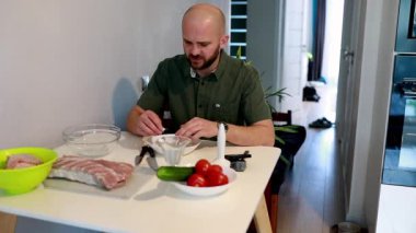 Bir şef, modern ve parlak bir mutfakta taze sebze ve et hazırlar. Salatalık ve domates gibi malzemeler, o yemek pişirme görevlerine odaklanırken masanın üzerinde düzgünce düzenlenir..