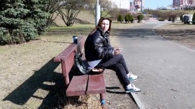 Parktaki bankta oturan bir kadın konteynırdan yemek yiyor. İçkisini yudumlarken etrafa bakıyor, dışarıda dinlenme gününün tadını çıkarıyor..