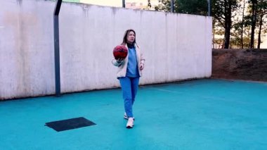 Genç bir kadın canlı mavi bir futbol sahasında elinde kırmızı bir topla duruyor ve yeteneklerini geliştiriyor. Tekniğini mükemmelleştirirken açık gökyüzü altında odaklanma ve kararlılık gösteriyor..
