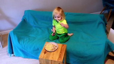 Küçük bir çocuk deniz mavisi bir kanepede oturur, ahşap bir masaya yerleştirilmiş aperatifin tadını çıkararak öğleden sonra oturma odasında rahat bir atmosfer yaratır..