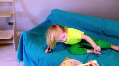 Parlak giysili genç bir çocuk rahat bir kanepeye uzanıyor, bir oyuncakla oynuyor ve evde bir kase abur cuburun tadını çıkarıyor. Sıcak atmosfer rahatlamaya ve oynamaya davet eder..