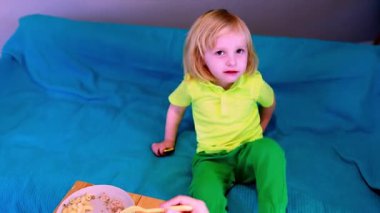 Parlak bir kıyafet giyen genç bir çocuk mutlu bir şekilde yemek yiyor. Bir el çatal üzerinde yemek sunar, ve ortam neşeli ve renklidir, yemek sırasında neşeli bir atmosfer yaratır..