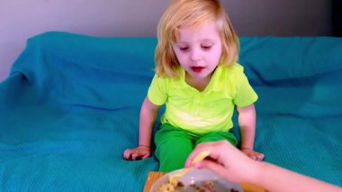 Parlak kıyafetler giyen genç bir çocuk kanepeye oturur, heyecanlı bir şekilde neşeli bir ifadeyle sağlıklı bir şeyler atıştırmaya çalışır. Samimi ortam neşeli bir atmosferi teşvik ediyor..