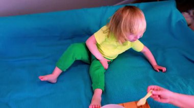 Canlı giyinmiş neşeli bir çocuk sıcak bir oturma odasında parlak mavi bir battaniyede neşeyle oynar. Özenli bir köpek yavrusu eğlenceyi uzaktan gözlemler ve iç açıcı bir sahne yaratır..