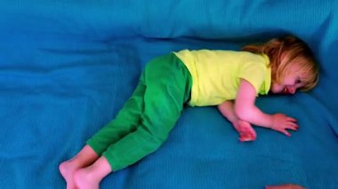 Parlak sarı gömlekli ve yeşil pantolonlu bir çocuk mavi bir kanepede neşeyle gülüp yuvarlanıyor. Yetişkin bir el görünür, cesaret verici bir etkileşimdir..